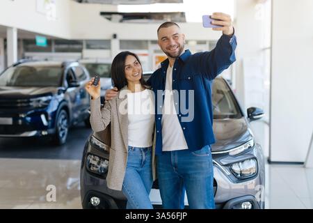 Cheerful couple taking selfie in car dealership showroom after purchasing new car Stock Photo