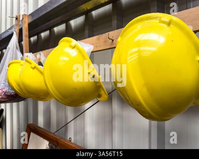 row of yellow protective hard hats safety helmets hanging on hooks at NELSAM north east land sea & air museum Stock Photo
