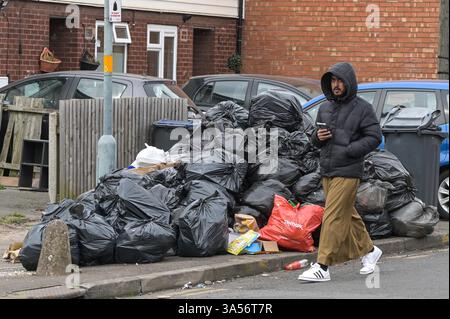 Calton Road, Birmingham 21st March 2025: A man walks past a large pile of rubbish bags on Carlton Road in the Bordesely Green area of Birmingham as council refuse workers continue to strike on every working day until their demands are met. Talks on Thursday evening between the council and Unite failed to resolve issues. Residents have complained that one mountain of waste has been festering for several weeks outside their homes. More than 350 refuse workers began industrial action in January over the scrapping of the safety critical Waste Recycling and Collection Officer (WRCO) role, resultin Stock Photo