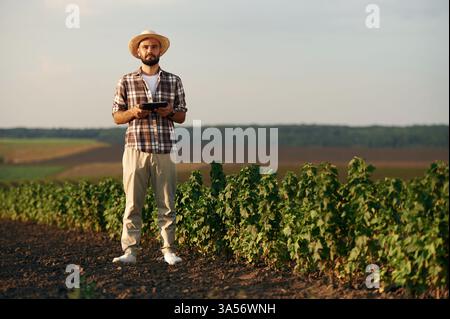 Standing and holding digital tablet. Farmer is on the agricultural field. Stock Photo