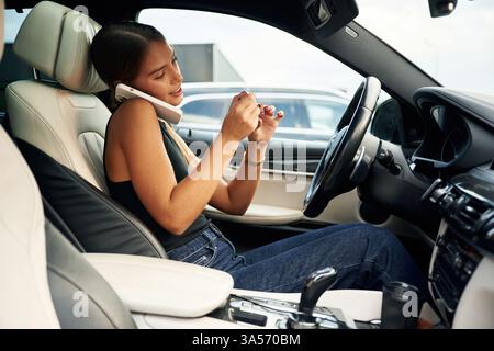 Side view, talking by phone. Woman is sitting in the car. Stock Photo