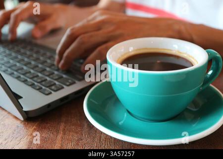 Closeup of a cup of coffee with a man working on laptop in the background Stock Photo