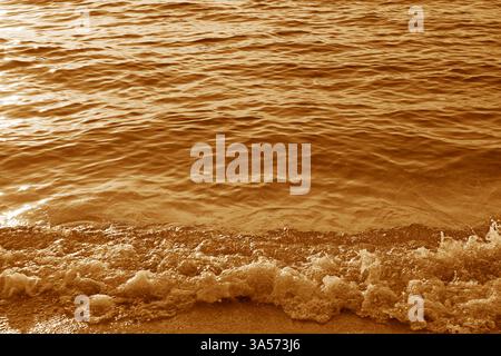 Golden waves in sunlight splashing on the beach Stock Photo