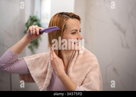 Woman combing her hair after shower in the bathroom Stock Photo