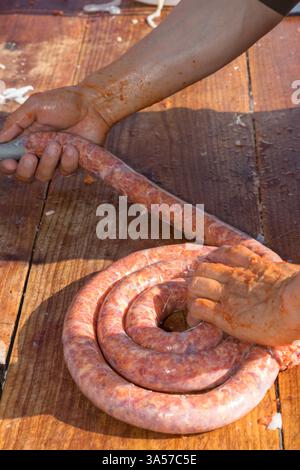 Close-up image depicting manual sausage-making process, hands handling raw sausage on a wooden surface. Stock Photo