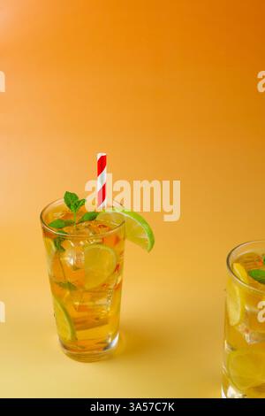 One glass of a ice tea with lime and lemon slices in it. The drink is served in a glass with mint leaves on the top and white and red straw. Stock Photo