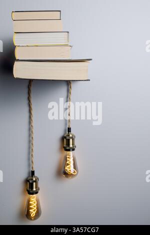 A shelf with books and two light bulbs hanging from it. The light bulbs are yellow and the books are stacked on top of each other. The scene gives off Stock Photo