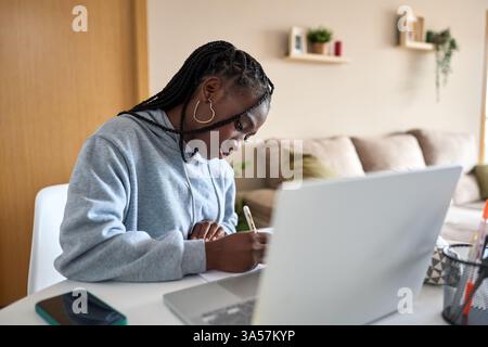 Focused student taking notes while studying online at home Stock Photo