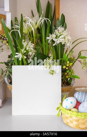 Decorative pot filled with lush green plants, white flowers and colorful Easter eggs in basket on a shelf with empty square, blank rectangle display c Stock Photo