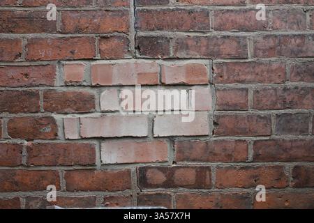 A brick wall with a white brick missing. The wall is made of red bricks Stock Photo