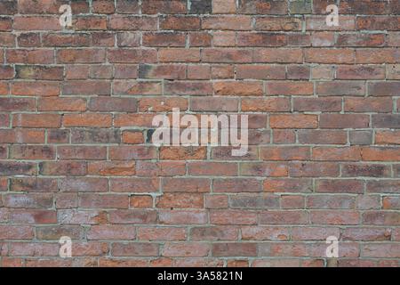 A brick wall with a few missing bricks. The wall is brown and has a rough texture. The missing bricks give the wall a somewhat unfinished look Stock Photo
