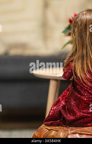 back of woman in red sequined dress sitting on brown leather ottoman Stock Photo