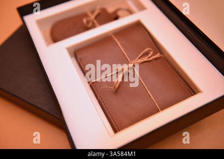 A close-up of a new natural brown leather wallet and key ring in the black box on a beige background Stock Photo