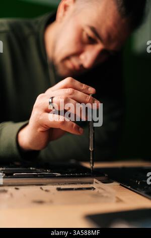 Vertical portrait of focused technician repairing laptop motherboard, carefully reassembling electronic components with precision screwdriver Stock Photo
