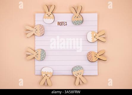 An Easter composition with a blank notebook sheet labeled 'Notes' surrounded by colourful rabbit clips on a soft pastel beige background Stock Photo