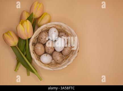 Easter Wicker Basket with White, Beige, and Brown Eggs and Pastel Yellow and Pink Tulips on Soft Beige Pink Background. Stock Photo