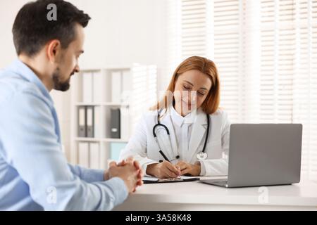 Cardiologist taking notes while consulting patient at table in clinic Stock Photo
