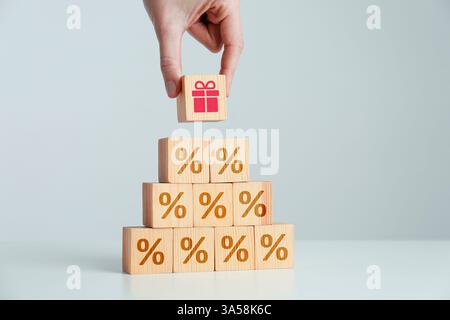 Bonus. Woman putting cube with gift box image on top of other ones with percent signs on light grey background, closeup Stock Photo