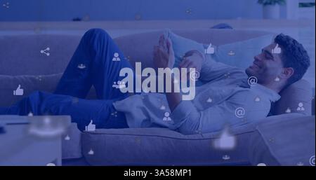Relaxing on couch, young man browsing smartphone with digital icons overlay Stock Photo