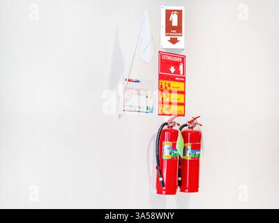A red fire extinguisher and flags placed below an exit sign on a white wall Stock Photo