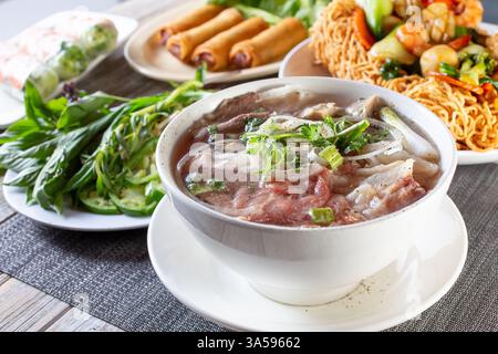 A view of a table full of a variety of Vietnamese dishes, featuring pho. Stock Photo