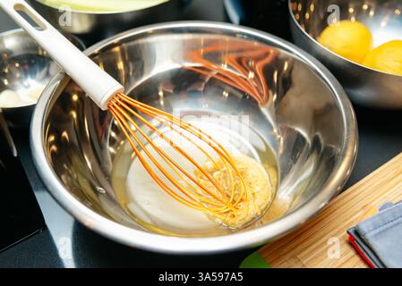 A stainless steel mixing bowl with a whisk and liquid ingredients, likely for baking or cooking, placed on a kitchen countertop with lemons nearby. Stock Photo