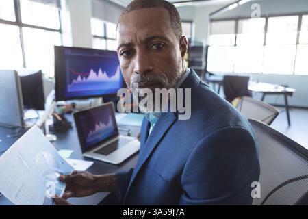 Businessman analyzing financial data on paper and computer in modern office Stock Photo