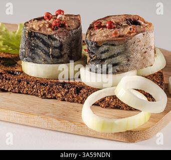 Sliced mackerel, chopped onion and a piece of black bread on a wooden kitchen board,close up Stock Photo