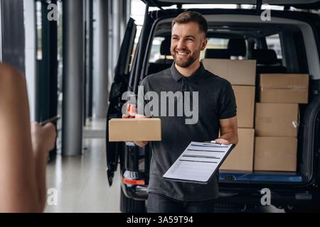 View from the back of female. Woman is taking her order from delivery man, with the car. Stock Photo