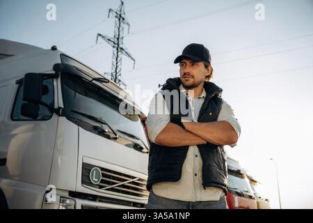 Serious facial expression, arms crossed. Truck driver is near the transport outdoors. Stock Photo