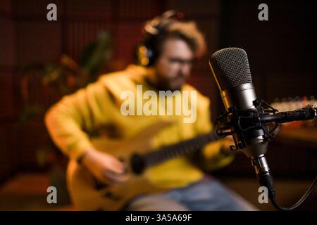 A focused male musician fine-tunes a bass guitar against the backdrop of a digital sound editing setup in a contemporary recording studio environment Stock Photo