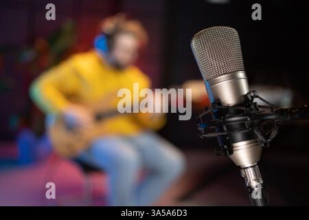 A focused male musician fine-tunes a bass guitar against the backdrop of a digital sound editing setup in a contemporary recording studio environment Stock Photo