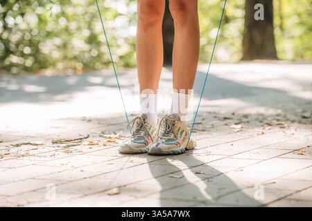 Legs of young woman that is using jumping rope. Outdoors, sunlight, close up view. Stock Photo