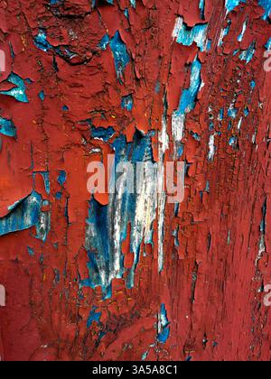 Close-up view of a weathered wooden surface displaying intricate patterns of peeling red and blue paint. The texture tells a story of age and exposure Stock Photo