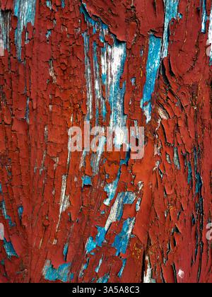Close-up view of a weathered wooden surface displaying intricate patterns of peeling red and blue paint. The texture tells a story of age and exposure Stock Photo