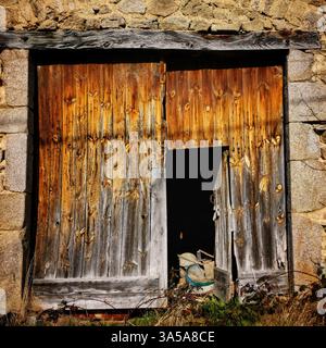 Rustic wooden barn door with weathered texture and overgrown grass at a rural location Stock Photo