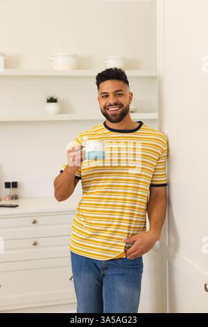 Smiling man in striped shirt enjoying coffee at home in modern kitchen Stock Photo
