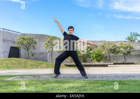 Dynamic young man striking a pose with outstretched arms in a park Stock Photo