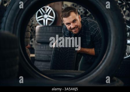 Looking through the hole in tire. Man worker is maintenance station with wheels. Stock Photo