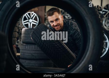 Looking through the hole in tire. Man worker is maintenance station with wheels. Stock Photo