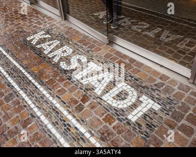 Freiburg, Germany - Feb 10, 2025: Mosaic letters forming the word Karstadt are inlaid into a cobblestone pavement at an entrance with glass doors and Stock Photo
