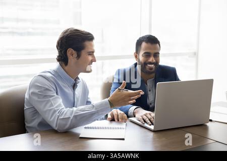 Teammates working on joint project seated at desk using laptop Stock Photo