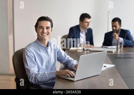 Smiling man sitting at desk with laptop, looking at camera Stock Photo