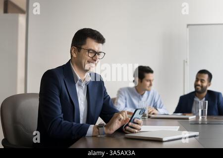Smiling mature businessman in suit sitting at desk using smartphone Stock Photo