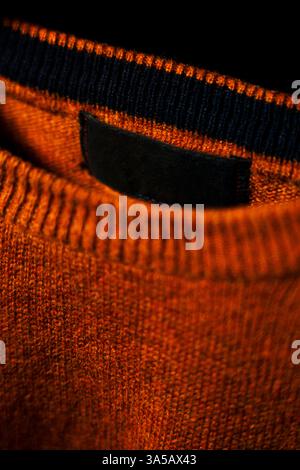 A close-up shot highlighting the soft fabric texture of a plain orange sweatshirt, displayed on a hanger against a black background. Perfect for empha Stock Photo