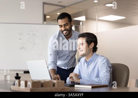Two smiling, positive teammates using laptop in meeting room Stock Photo