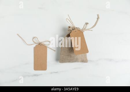 Burlap bag with tags on white marble table, flat lay Stock Photo