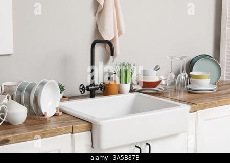 Stylish ceramic sink and clean dishes on wooden kitchen counter Stock Photo