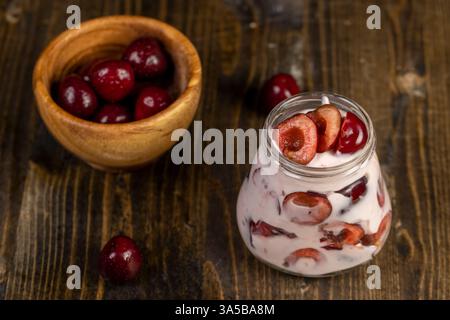 yogurt with cherry flavor closeup, jar with cherry yogurt with fresh red cherries, red berries in a wooden bowl Stock Photo