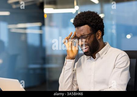 A young African American businessman in an office is experiencing a stressful day, looking frustrated while trying to work. Stock Photo